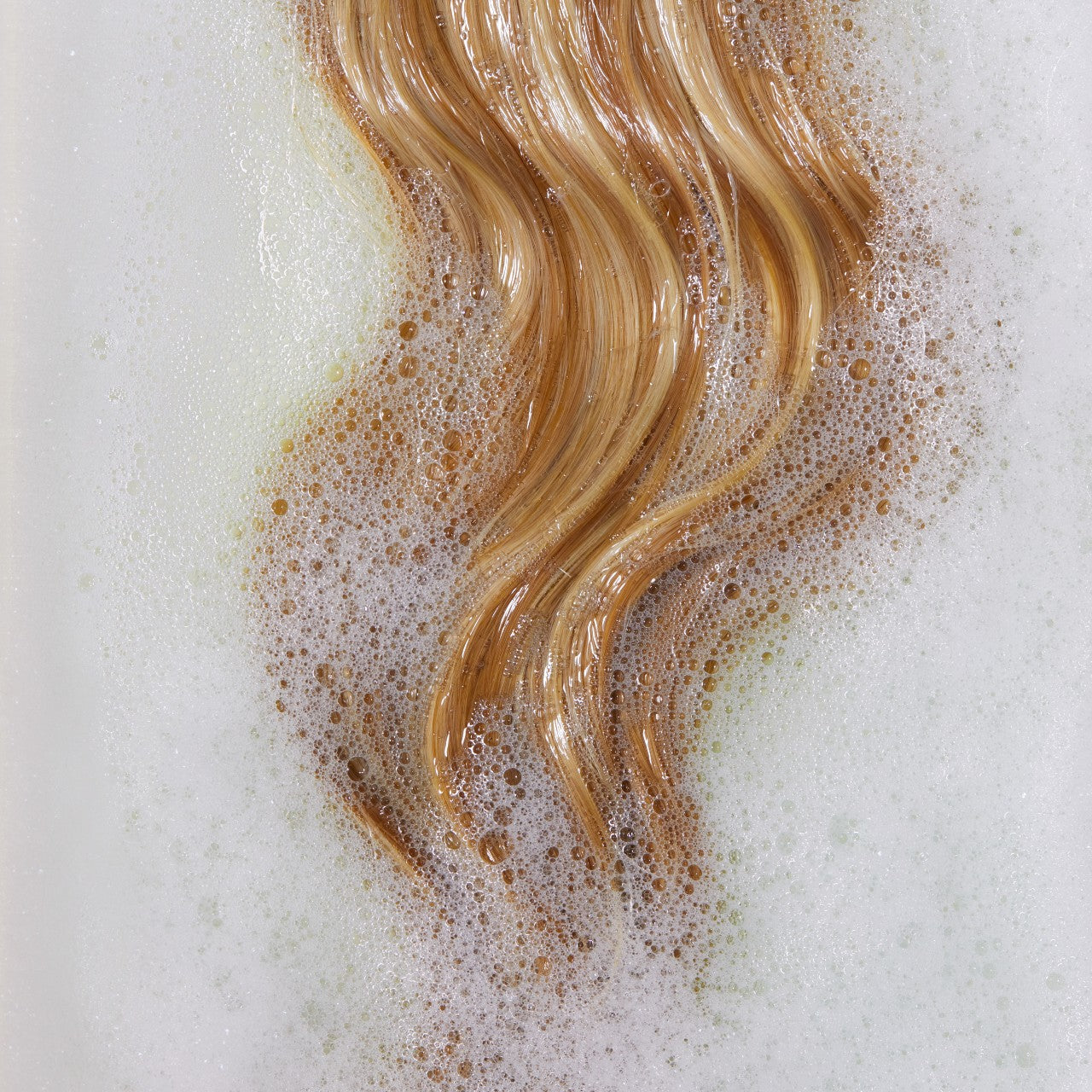 Long blonde hair laying in bath among soap suds